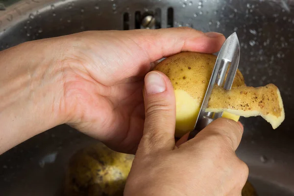 Mulher mão descascando batata na pia com faca descascador — Fotografia de Stock