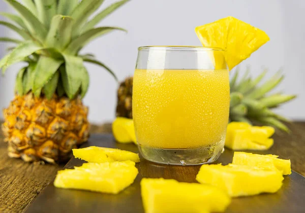 A glass of pineapple juice with pineapple slice on wooden table background.