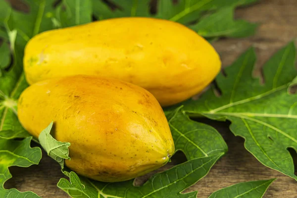 Close up papaya with papaya leaf on wooden table background.