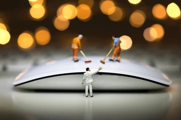Bokeh arka planında beyaz bir bilgisayar faresini temizleyen minyatür figür.