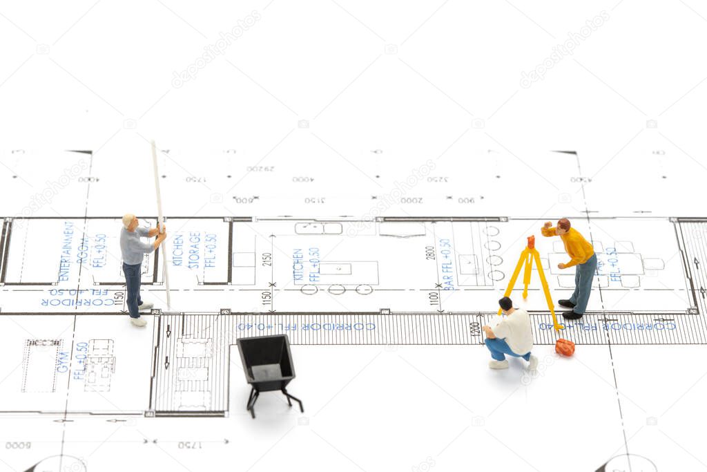 Miniature people surveyor technician is measuring the distance to build a house on drawing plan.