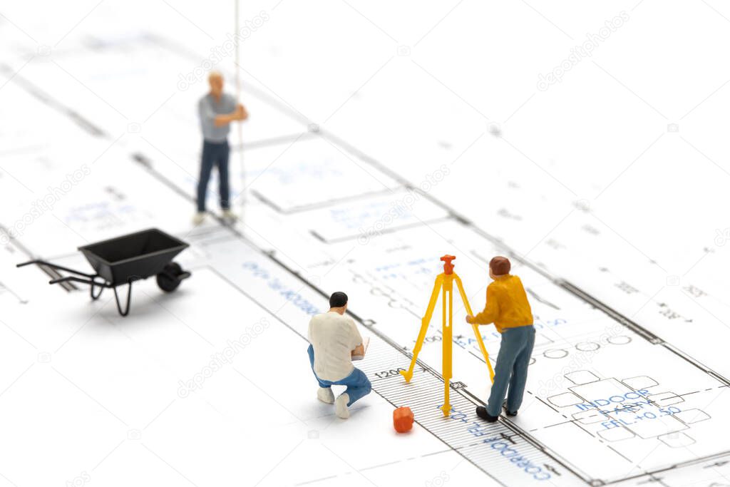 Miniature people surveyor technician is measuring the distance to build a house on drawing plan.