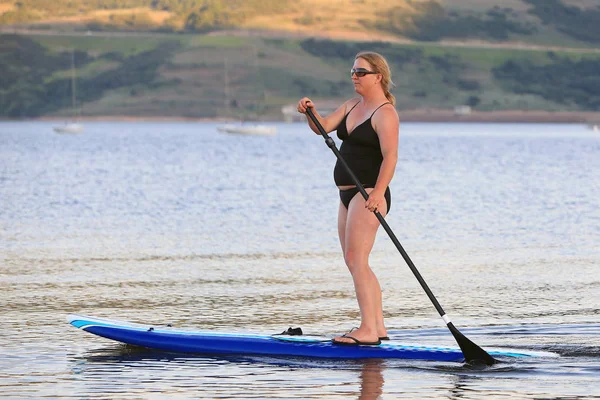 woman on a stand up paddleboard on a lake at dusk, Utah, USA