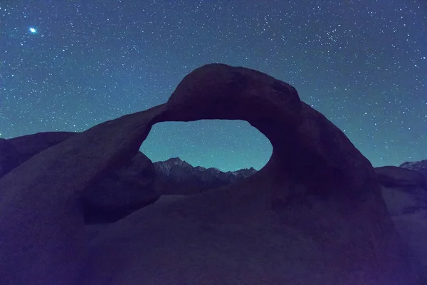 Night scene with Starry sky above a granite arch in the Eastern Sierra Mountains, California, USA.