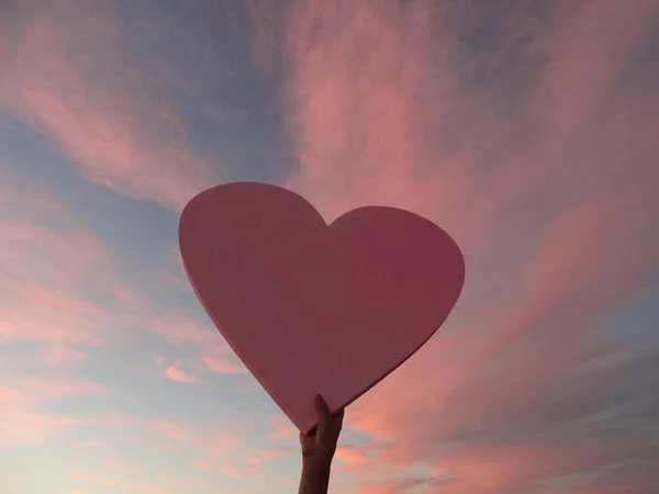 Female Hand holding a big Pink Heart on the Background of a Pink