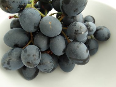 Beyaz arka plan üzerinde beyaz bir kase içinde siyah üzüm