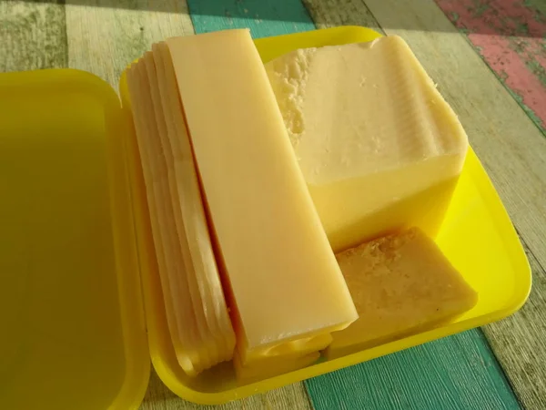 在复古木桌上的黄色塑料盒中的黄色奶酪 — 图库照片