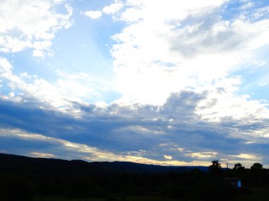 Mavi gökyüzünde beyaz bulutlar arkasında güneş ışığı