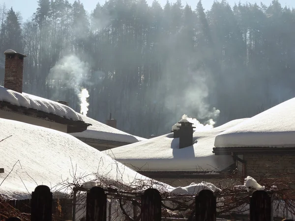 Tetti della casa coperti di neve e fumo dai camini — Foto Stock