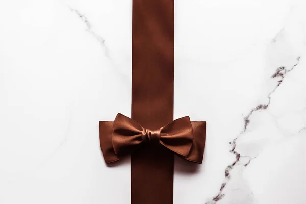 Chocolate brown silk ribbon on marble background, flatlay