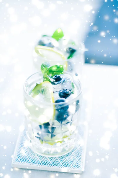 Winter holiday cocktail with ice and glowing snow on background,