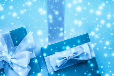 Kış tatili hediyeleri ve dondurulmuş mavi arka planda parlayan kar,