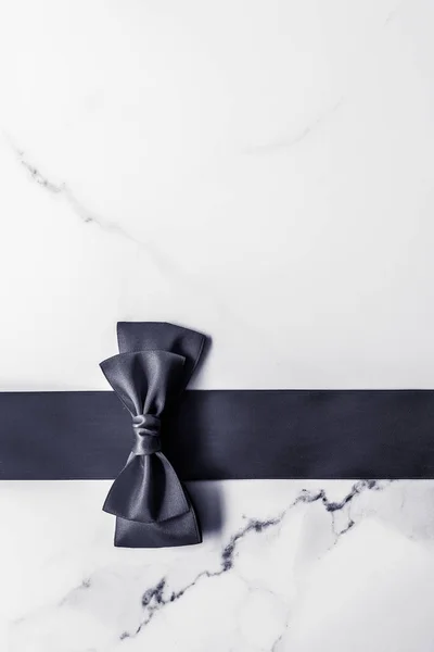 Black silk ribbon and bow on marble background, flatlay