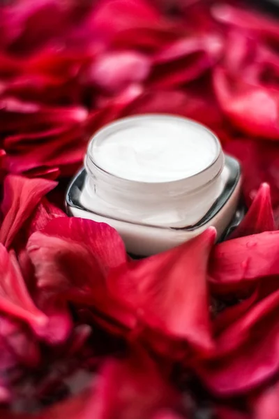 Crema hidratante para el cuidado de la piel sensible sobre pétalos de flores rojas y wa — Foto de Stock