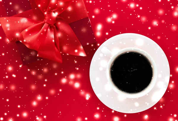 Winter holiday gift box, coffee cup and glowing snow on red flat