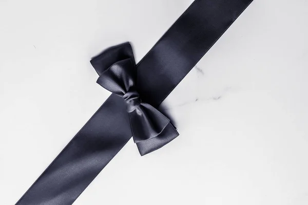 Black silk ribbon and bow on marble background, flatlay