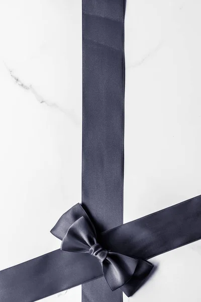 Black silk ribbon and bow on marble background, flatlay