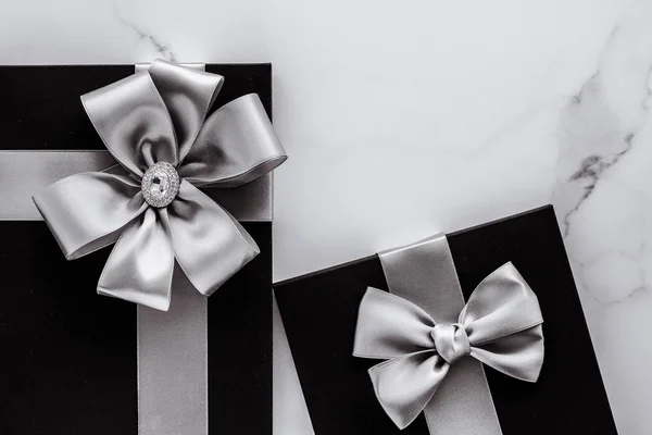 Роскошные праздничные подарки с серебряной шелковой лентой и луком на мраморе b — стоковое фото