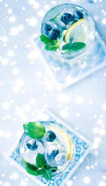 Winter holiday cocktail with ice and glowing snow on background,