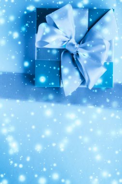 Kış tatili hediyeleri ve dondurulmuş mavi arka planda parlayan kar,