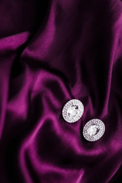 深粉色真丝织物上的豪华钻石耳环，节日玻璃 — 图库照片