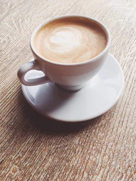 Ένα φλιτζάνι ζεστό καπουτσίνο σε μια καφετέρια, καφέ σε ένα ξύλινο τραπέζι που — Φωτογραφία Αρχείου
