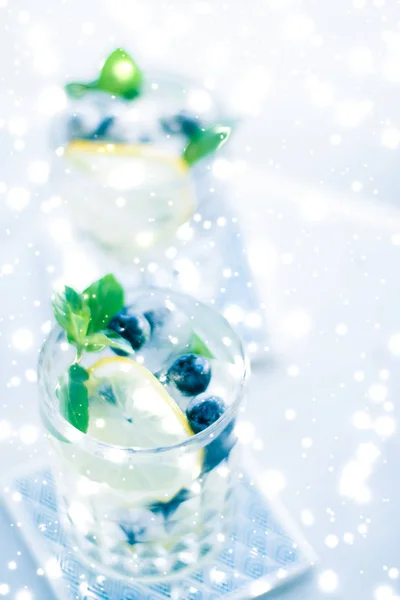 Winter holiday cocktail with ice and glowing snow on background,