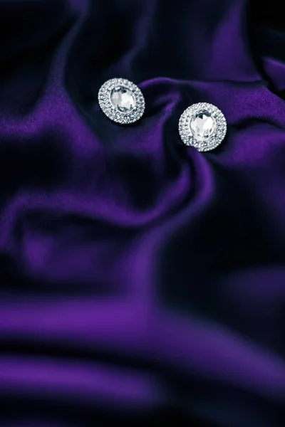 Роскошные бриллиантовые серьги на темно-фиолетовой шелковой ткани, праздничный глэм — стоковое фото