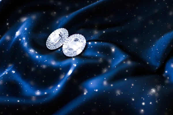 Luxury diamond earrings on dark blue silk with snow glitter, hol