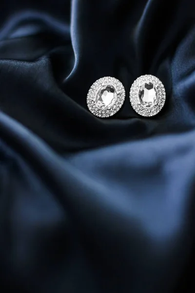 Luxury diamond earrings on dark blue silk background, holiday gl