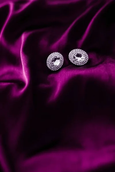 Luxusní diamantové náušnice na tmavě růžovém hedvábném tkanině, prázdninové glamou — Stock fotografie