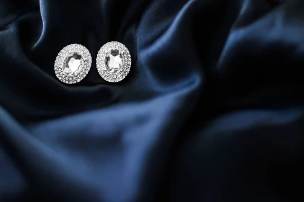 ダークブルーシルクの背景に豪華なダイヤモンドのイヤリング、ホリデーgl — ストック写真