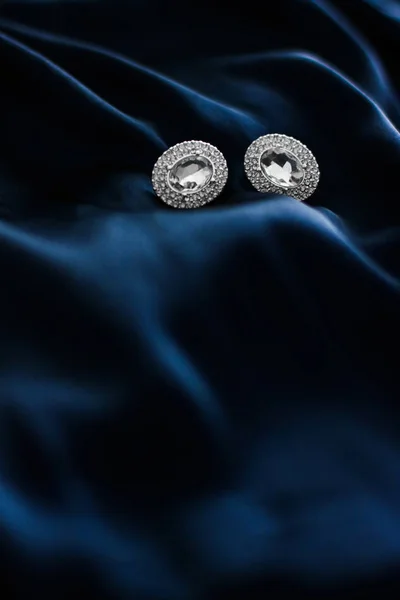 Luxury diamond earrings on dark blue silk background, holiday gl