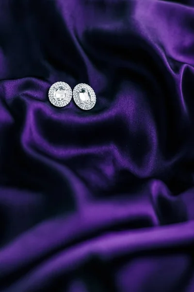 Luxury diamond earrings on dark violet silk fabric, holiday glam