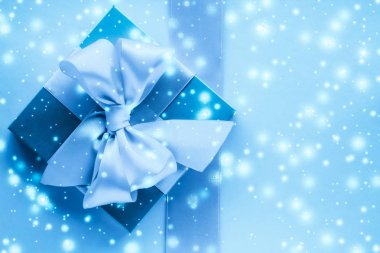 Kış tatili hediyeleri ve dondurulmuş mavi arka planda parlayan kar,