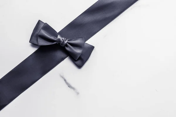 Black silk ribbon and bow on marble background, flatlay — Stock Photo, Image