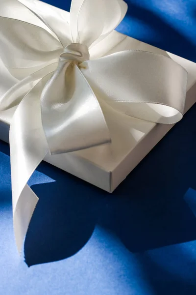 Luksusowe wakacje biały prezent pudełko z jedwabną wstążką i łuk na niebieskim b — Zdjęcie stockowe