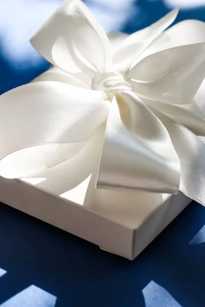 Luksusowe wakacje biały prezent pudełko z jedwabną wstążką i łuk na niebieskim b — Zdjęcie stockowe