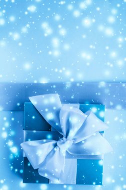Kış tatili hediyeleri ve dondurulmuş mavi arka planda parlayan kar,