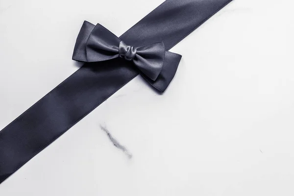 Black silk ribbon and bow on marble background, flatlay