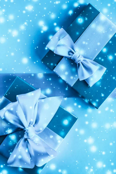 Winter holiday gifts and glowing snow on frozen blue background,