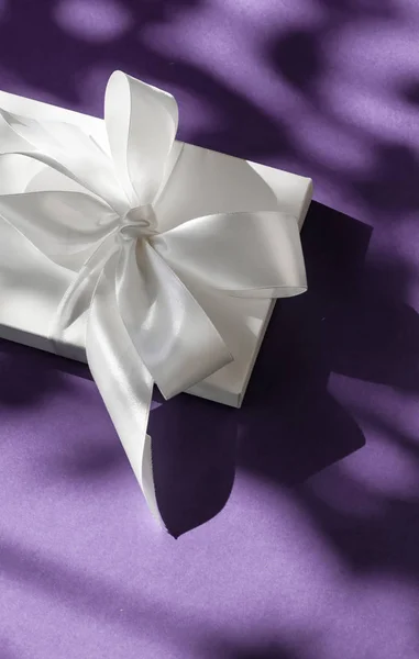 Luxury holiday white gift box with silk ribbon and bow on violet