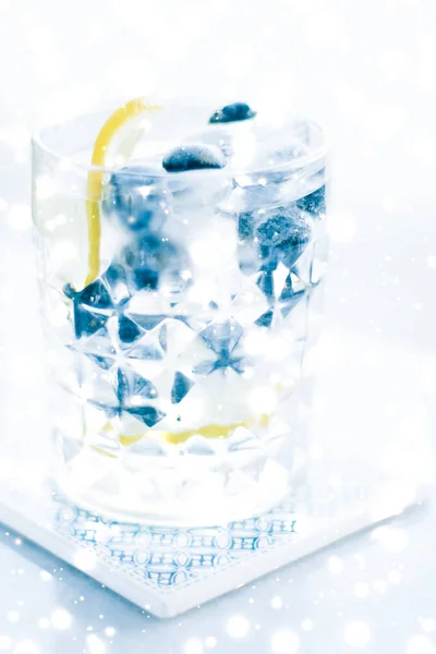 Winter holiday cocktail with ice and glowing snow on background,