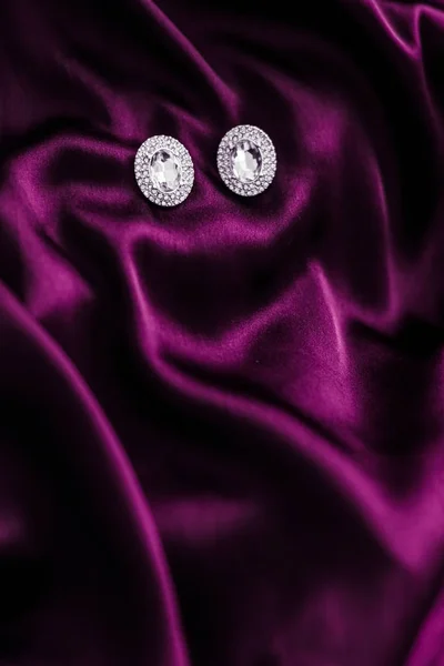 Luxusní diamantové náušnice na tmavě růžovém hedvábném tkanině, prázdninové glamou — Stock fotografie
