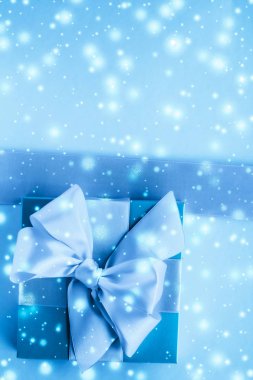 Kış tatili hediyeleri ve dondurulmuş mavi arka planda parlayan kar,