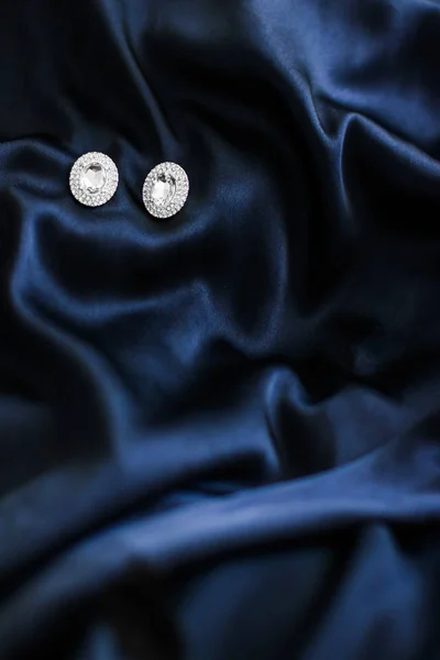 Luxury diamond earrings on dark blue silk background, holiday gl