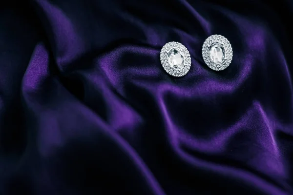 Luxury diamond earrings on dark violet silk fabric, holiday glam — Stock Photo, Image