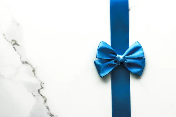 Blue silk ribbon and bow on luxury marble background, holiday fl