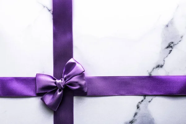 Purple silk ribbon and bow on luxury marble background, holiday