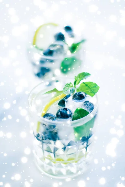 Winter holiday cocktail with ice and glowing snow on background,